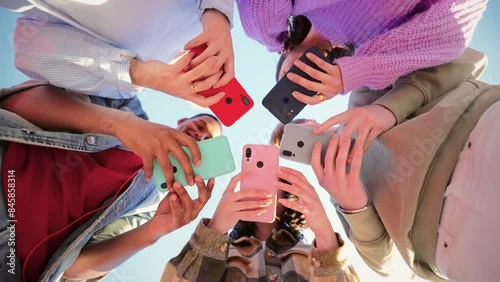 Low angle view of a group of unrecognizable multiracial young friends using their cellphones on a circle. Team of teenagers enjoying and browsing on internet with a smart phone application.