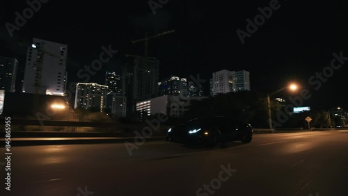 Rolling shot of  black supercar driving at night on the streets in Miami Florida city with skyline city lights view