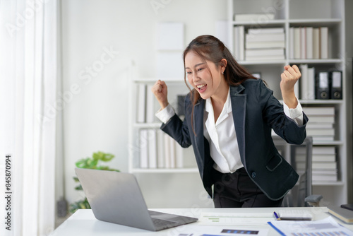 Cheerful businesswoman celebrating success at her workplace, expressing excitement and achievement in a modern office environment.