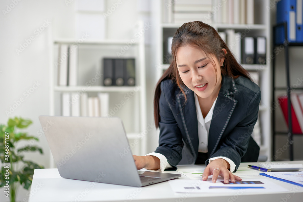Confident businesswoman working on laptop in modern office, analyzing documents, and smiling, representing success and productivity. Confident businesswoman working on laptop in modern office, analyzing documents, and smiling, representing success and productivity.