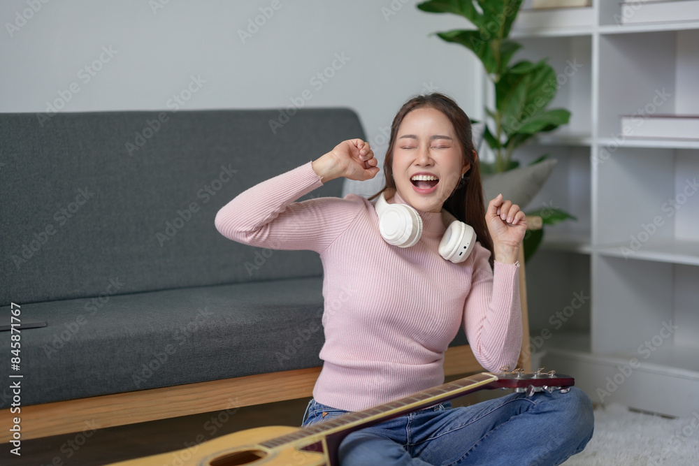 Young woman enjoying music with headphones, sitting on the floor near a guitar, happily singing in a modern living room. Young woman enjoying music with headphones, sitting on the floor near a guitar, happily singing in a modern living room.