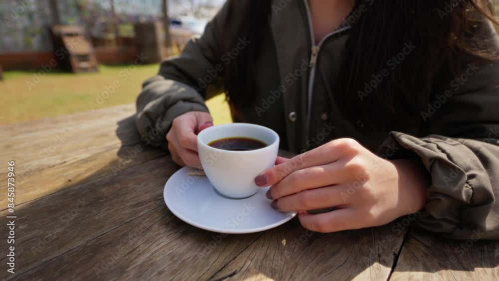 Close-Up of Female Hands Holding a Coffee Cup on a Wooden Table in a Rural Environment. Woman Holding Coffee Cup in Rustic Outdoor Setting Close-Up of Female Hands Holding a Coffee Cup on a Wooden Table in a Rural Environment. Woman Holding Coffee Cup in Rustic Outdoor Setting