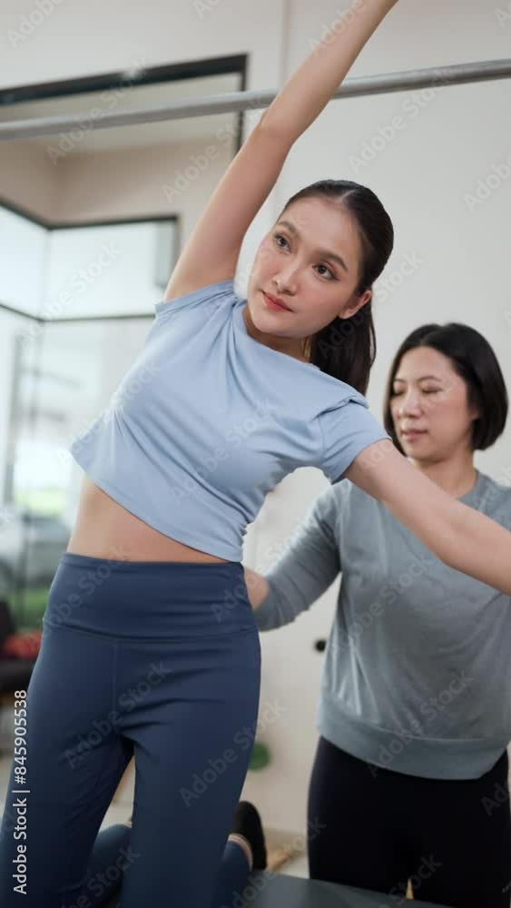Asian Woman in sport outfit exercising by bend body her side down Young woman stretching and pilates instructor holding her gently In order to strengthen core body and spine correcting Asian Woman in sport outfit exercising by bend body her side down Young woman stretching and pilates instructor holding her gently In order to strengthen core body and spine correcting