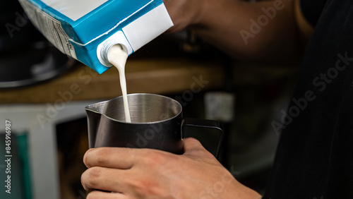 Close-up of hands pouring milk into pitcher for gourmet coffee