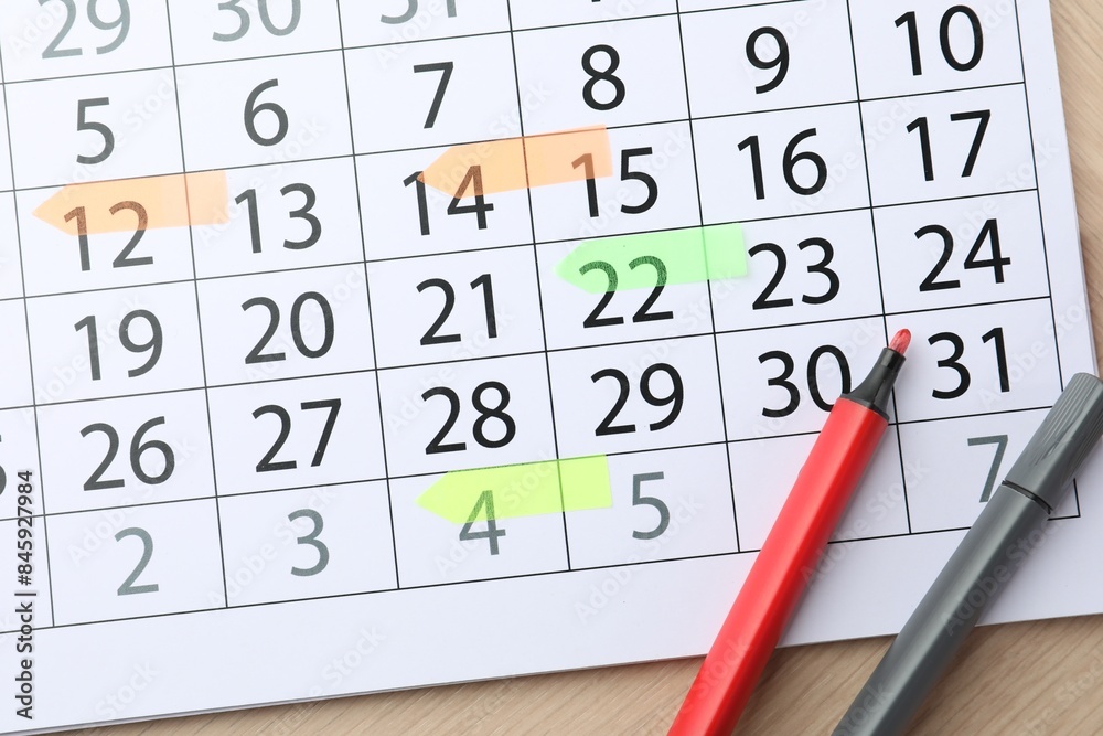 Timetable. Calendar page with marked dates and felt pens on wooden table, top view Timetable. Calendar page with marked dates and felt pens on wooden table, top view