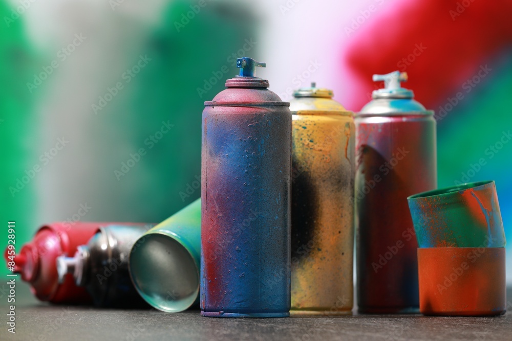 Many spray paint cans on gray surface against color background Many spray paint cans on gray surface against color background