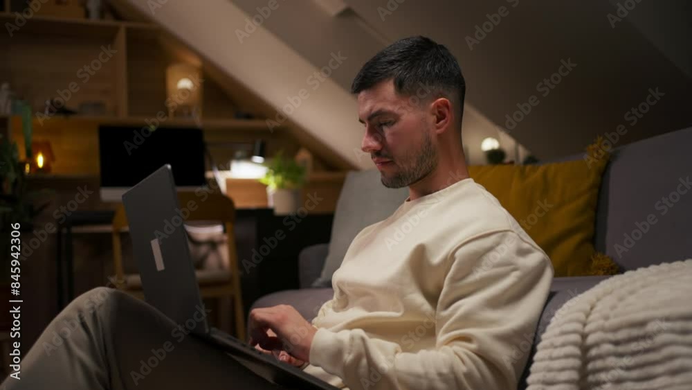 Handsome man resting on sofa at home, using laptop computer to watch videos on the Internet