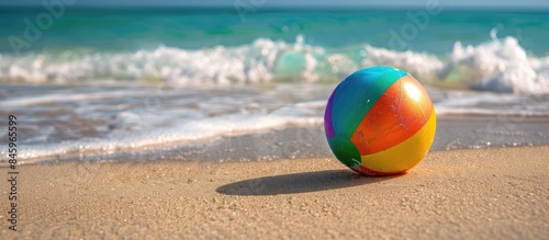 Vivid colored ball resting on damp sand by the rippling sea under the sunny skies at Parrot Beach. #845965599