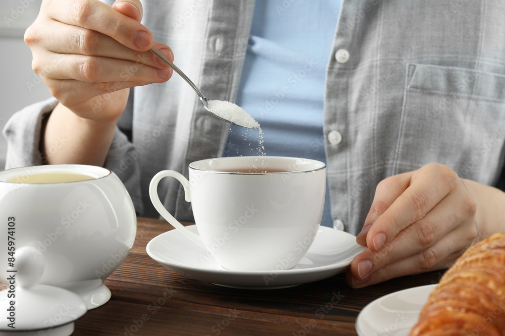 Woman adding sugar into cup of tea at wooden table, closeup Woman adding sugar into cup of tea at wooden table, closeup