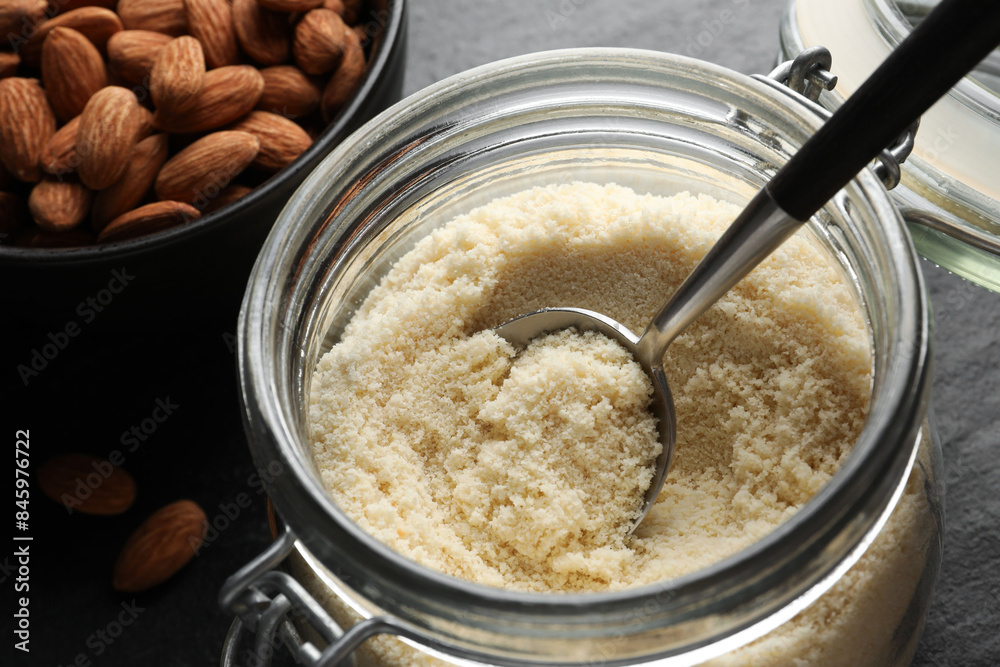 Fresh almond flour, spoon in jar and nuts on dark table, closeup Fresh almond flour, spoon in jar and nuts on dark table, closeup