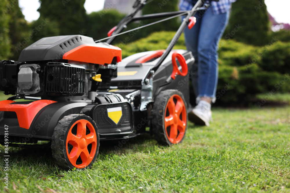 Obraz premium Woman cutting green grass with lawn mower in garden, selective focus