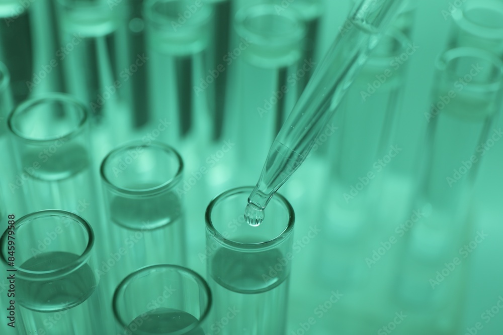Dripping liquid from pipette into test tube on green background, closeup Dripping liquid from pipette into test tube on green background, closeup
