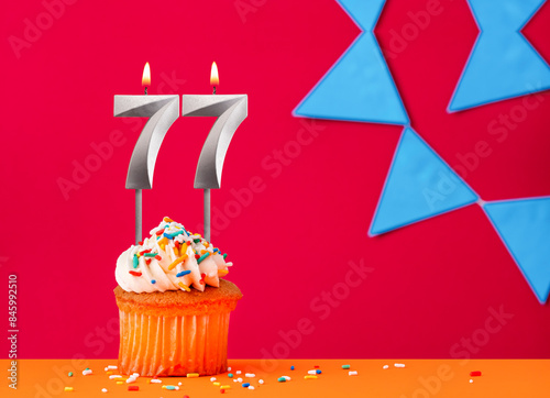 Birthday cupcake with candle number 77 on a red background with blue pennants