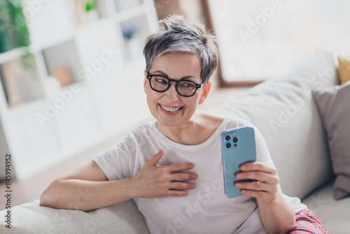 Photo of lovely mature lady hold gadget video call dressed white garment modern living room rest enjoy weekend free leisure time alone home