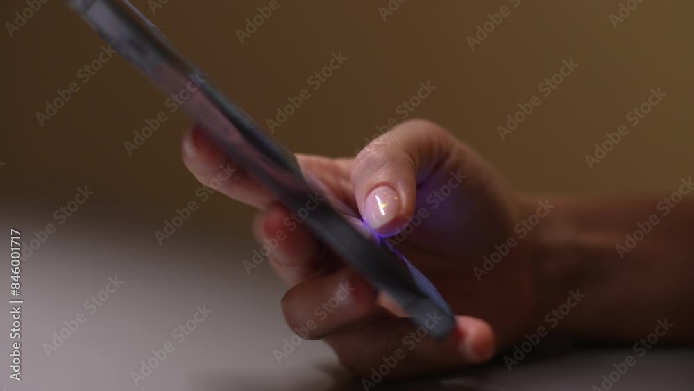 Side view of unrecognizable woman holding smartphone, using mobile applications, chatting with friends in social networks, playing online game, web surfing or shopping, sitting at desk in dark room.