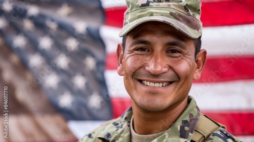 Smiling soldier in camouflage uniform against blurred American flag background for patriotic themes. photo