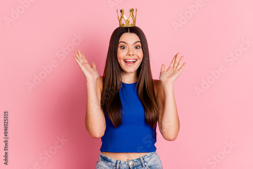 Photo of cheerful excited lady dressed blue top gold tiara rising arm empty space isolated pink color background
