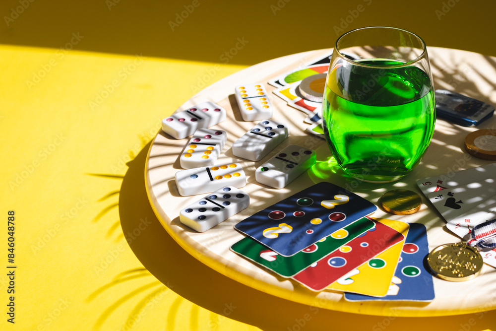Fototapeta premium White dominoes, playing cards, uno, ligretto and a green drink on a yellow background. Board game.