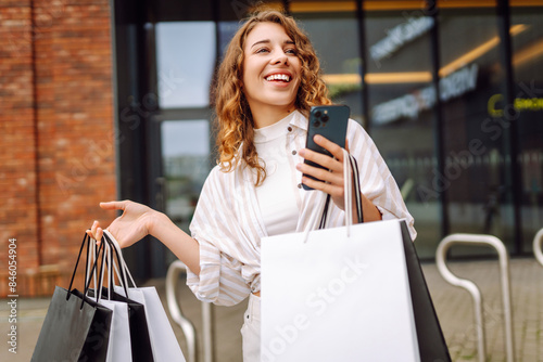 Young Woman use of mobile phone and hold with shopping bag. Consumerism, sale, black friday. Online shopping.