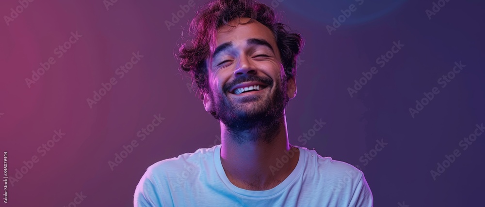 A young man with a beard smiles brightly, bathed in blue and purple light. A young man with a beard smiles brightly, bathed in blue and purple light.
