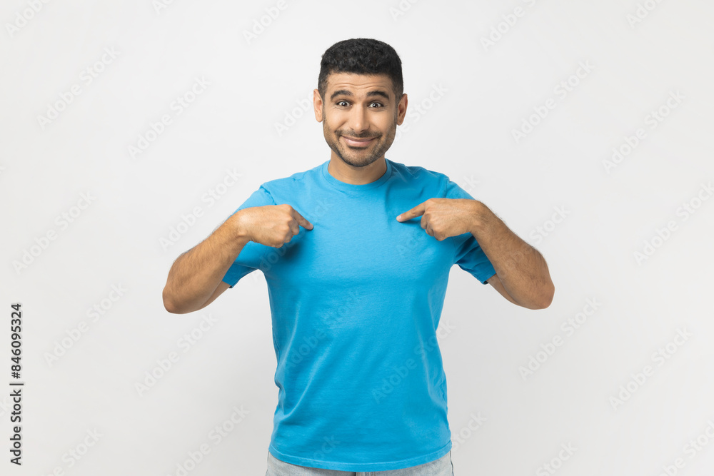 Portrait of smiling satisfied unshaven man indicates at himself, feels proud of personal achievements, has positive face and rejoicing. Indoor studio shot isolated on gray background. Portrait of smiling satisfied unshaven man indicates at himself, feels proud of personal achievements, has positive face and rejoicing. Indoor studio shot isolated on gray background.