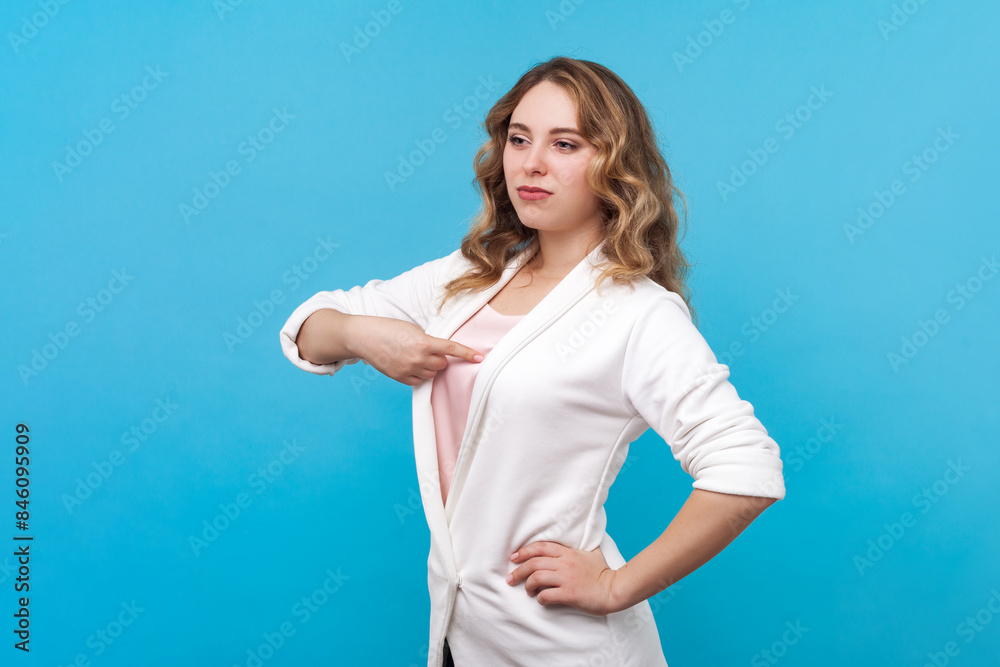 Portrait of proud self confident egoistic blond woman with wavy hair pointing at herself with arrogant expression, wearing white shirt. Indoor studio shot isolated on blue background. Portrait of proud self confident egoistic blond woman with wavy hair pointing at herself with arrogant expression, wearing white shirt. Indoor studio shot isolated on blue background.