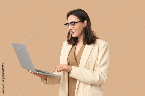 Young businesswoman with laptop on beige background