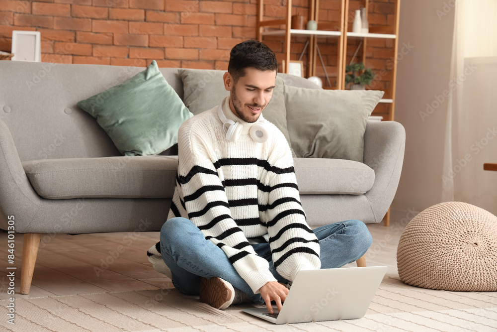 Obraz premium Handsome young happy man with laptop resting on floor at home