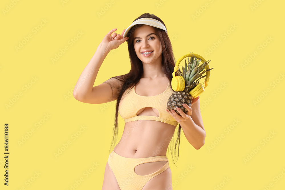 Portrait of pretty young woman in swimsuit with pineapple and headphones on yellow background Portrait of pretty young woman in swimsuit with pineapple and headphones on yellow background