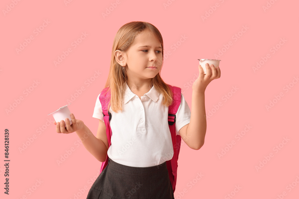 Thoughtful little schoolgirl with backpack and yogurts on pink background Thoughtful little schoolgirl with backpack and yogurts on pink background