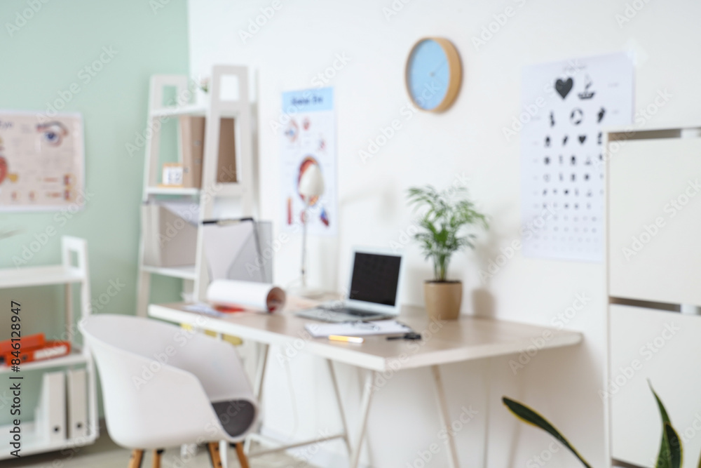 Blurred view of ophthalmologist's office with workplace and eye test chart Blurred view of ophthalmologist's office with workplace and eye test chart
