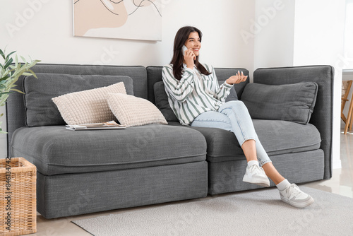 Young woman talking with mobile phone on black sofa in living room