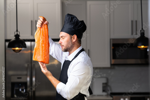 A chef is holding a piece of salmon in his hand and wearing a black hat. High quality photoA chef is holding a piece of salmon in his hand and wearing a black hat. Concept expertise in the kitchen photo
