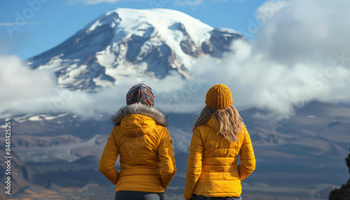 Two Adventurous Hikers in Vibrant Yellow Jackets Gazing at a Snow Capped Mountain Amidst a Majestic Landscape of Rocky Terrain and Rolling Clouds in a Serene Adventure