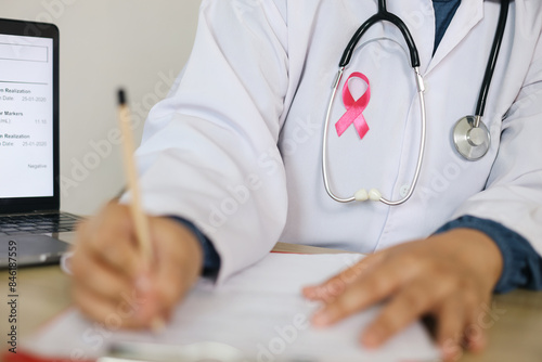 Doctor With White Coat Writting On Medical Document Wearing Pink Ribbon And Stethoscope photo