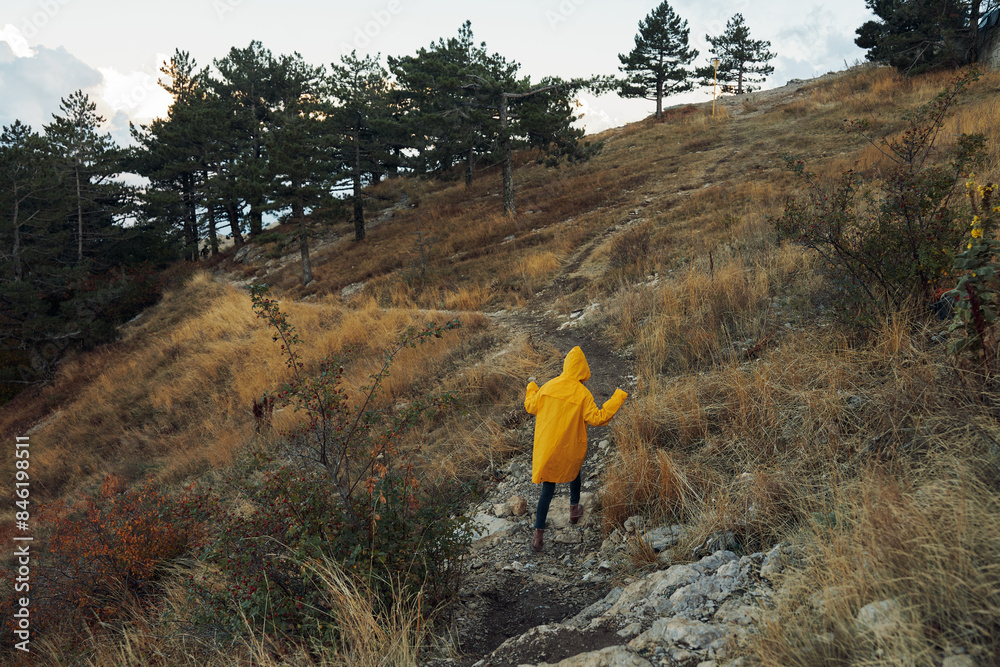 Naklejka premium A person wearing a yellow raincoat walking up a steep hill with an umbrella in hand on a rainy day