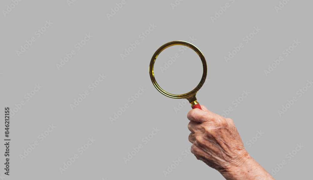 Close-up of an old woman's hand holding a magnifying glass against a gray background. Close-up of an old woman's hand holding a magnifying glass against a gray background.