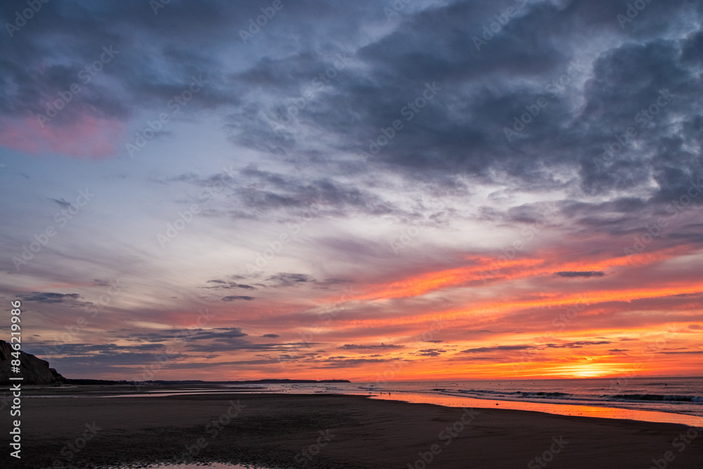 Captured at dusk, this image showcases a beautiful sunset over an expansive beach with colorful skies.