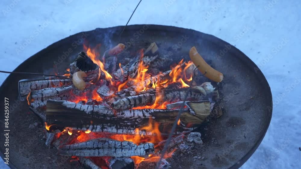 Roasting sausages on sticks over a warm, roaring fire, cozy winter outdoor cookout Roasting sausages on sticks over a warm, roaring fire, cozy winter outdoor cookout