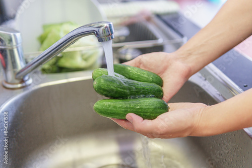Woman hands washing fresh green baby cucumbers in kitchen