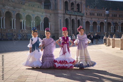 Four girls dancing flamenco, posing looking at camera, wearing typical flamenco dress in a nice square in Seville. Dance concept, flamenco, typical Spanish, Seville, Spain.