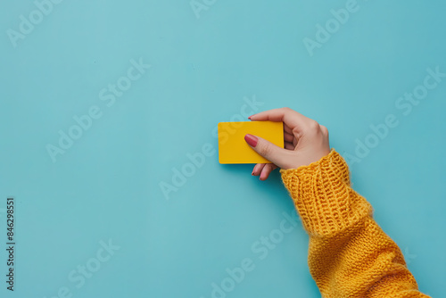 Close-up of a woman's hand holding a yellow credit card against a light blue background, representing financial transactions and payment options photo