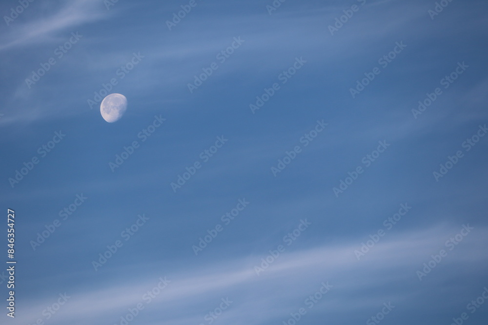 Daytime moon shines in clear blue sky with light clouds, creating serene atmosphere in nature Daytime moon shines in clear blue sky with light clouds, creating serene atmosphere in nature