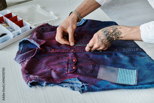 Bild auf Leinwand A young man with tattoos works on a discarded denim shirt, giving it new life with sustainable clothing restoration