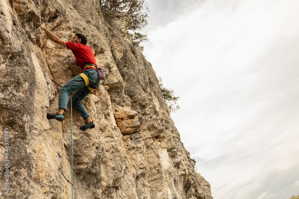 A man is climbing a rock wall with a red shirt and blue pants