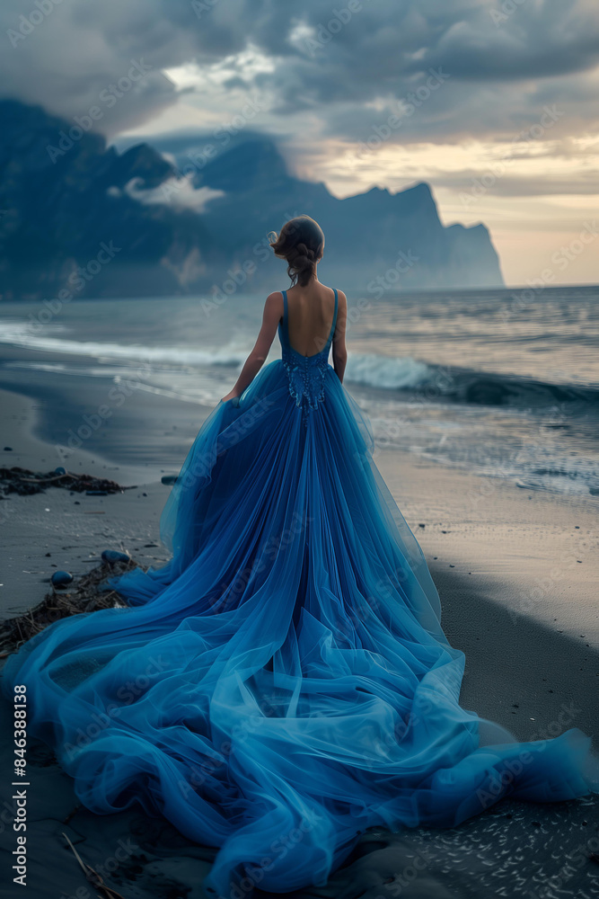 blonde woman in blue tulle dress standing on the beach, fantasy landscape with mountains and sea, prom dress rental, fantasy photoshoot