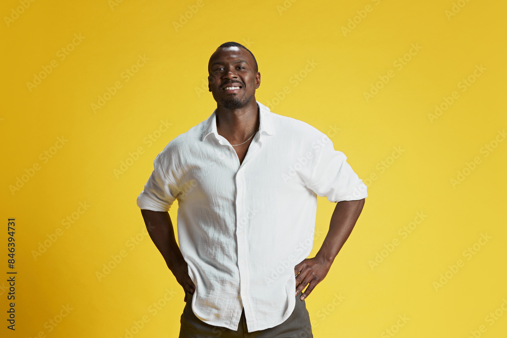 Portrait of smiling young African-American man posing and looking at camera against bright yellow background. Happiness and positive mood. Concept of human emotions facial expression, fashion Portrait of smiling young African-American man posing and looking at camera against bright yellow background. Happiness and positive mood. Concept of human emotions facial expression, fashion
