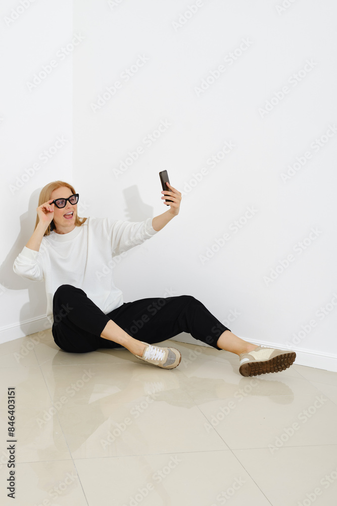Fototapeta premium Funny woman sits on a floor and making selfie with smartphone