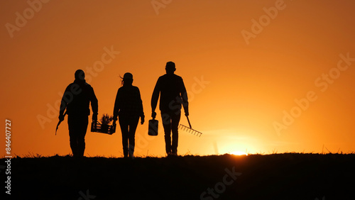 Three farmers  accompanied by their equipment  stroll through a field as the sun sets.