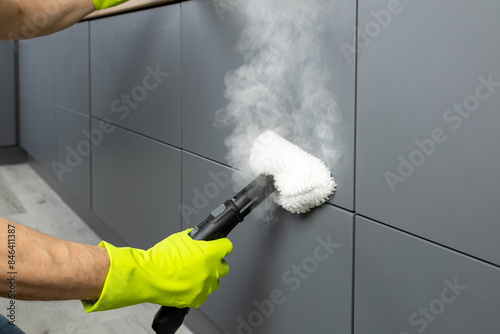 A man's hand in a protective glove cleans the kitchen facade with steam